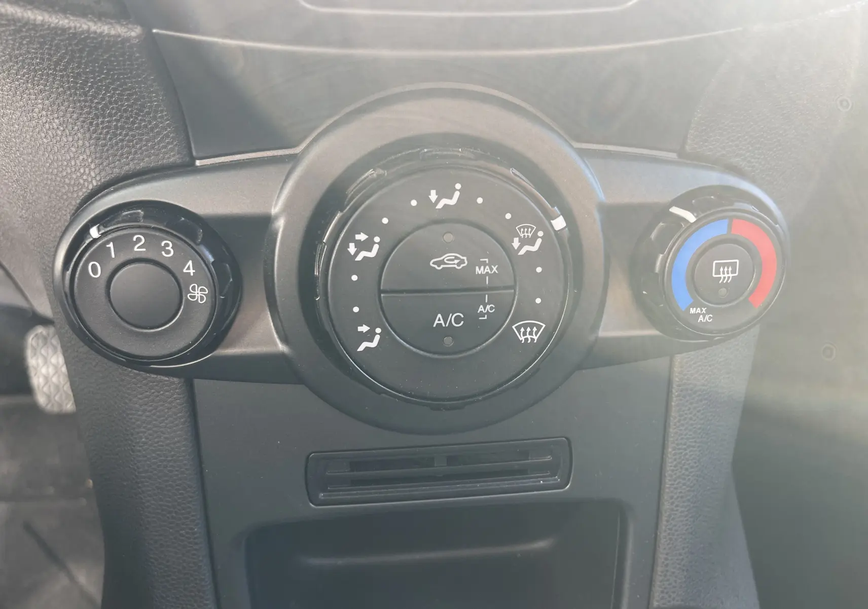 Gros plan sur les commandes de climatisation d'une Ford Fiesta gris titane 2014 avec réglages manuels et bouton de chauffage arrière.