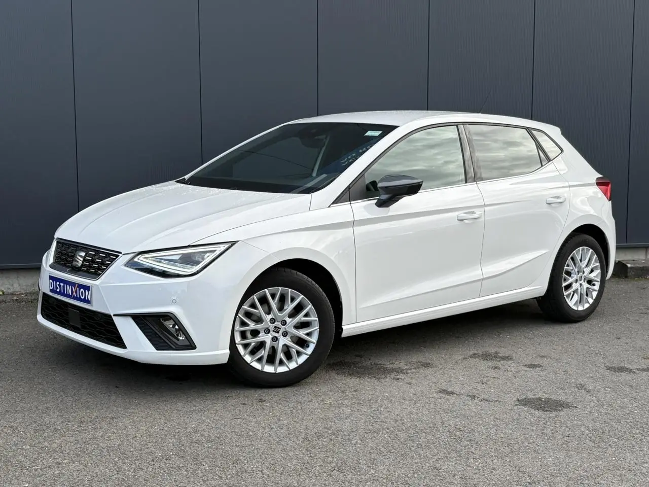 SEAT Ibiza TSI 115 Xcellence blanc vue 3/4 avant avec jantes alliage et rétroviseurs noirs sur fond urbain.