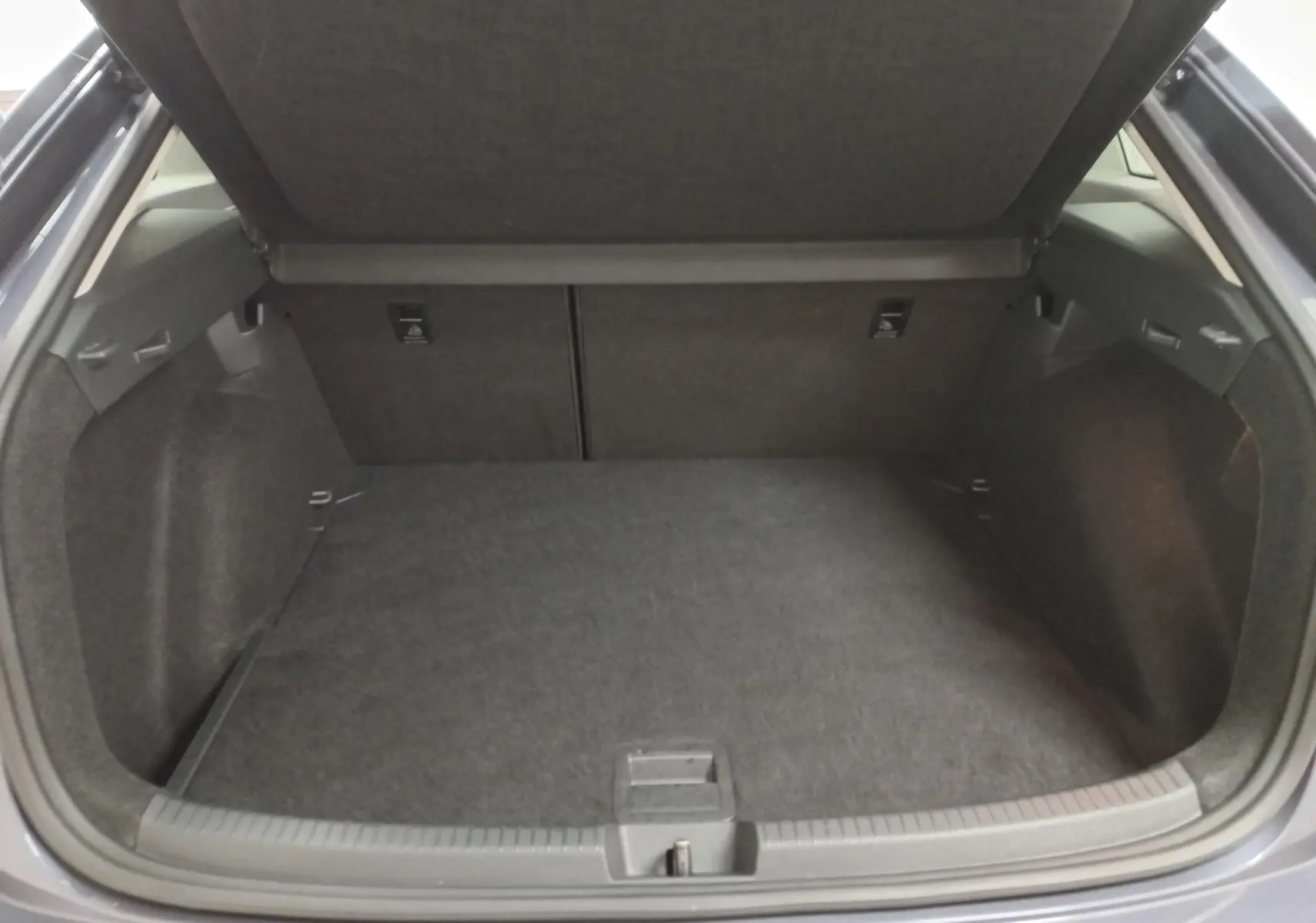 Coffre ouvert vu de l'arrière d'un Volkswagen Taigo gris cendré, montrant un espace de chargement vide et propre.