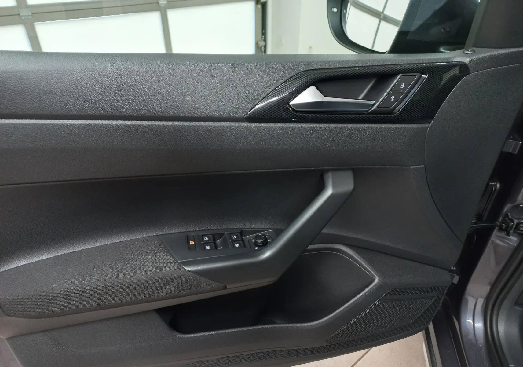 Vue intérieure côté gauche de la porte avant d'une Volkswagen Taigo gris cendré avec commandes électriques et poignée noire.