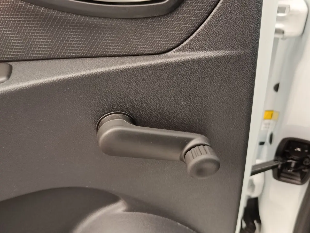 Détail de la manivelle de lève-vitre côté gauche sur porte intérieure noire d’une Renault Clio Business dCi 75 blanche.