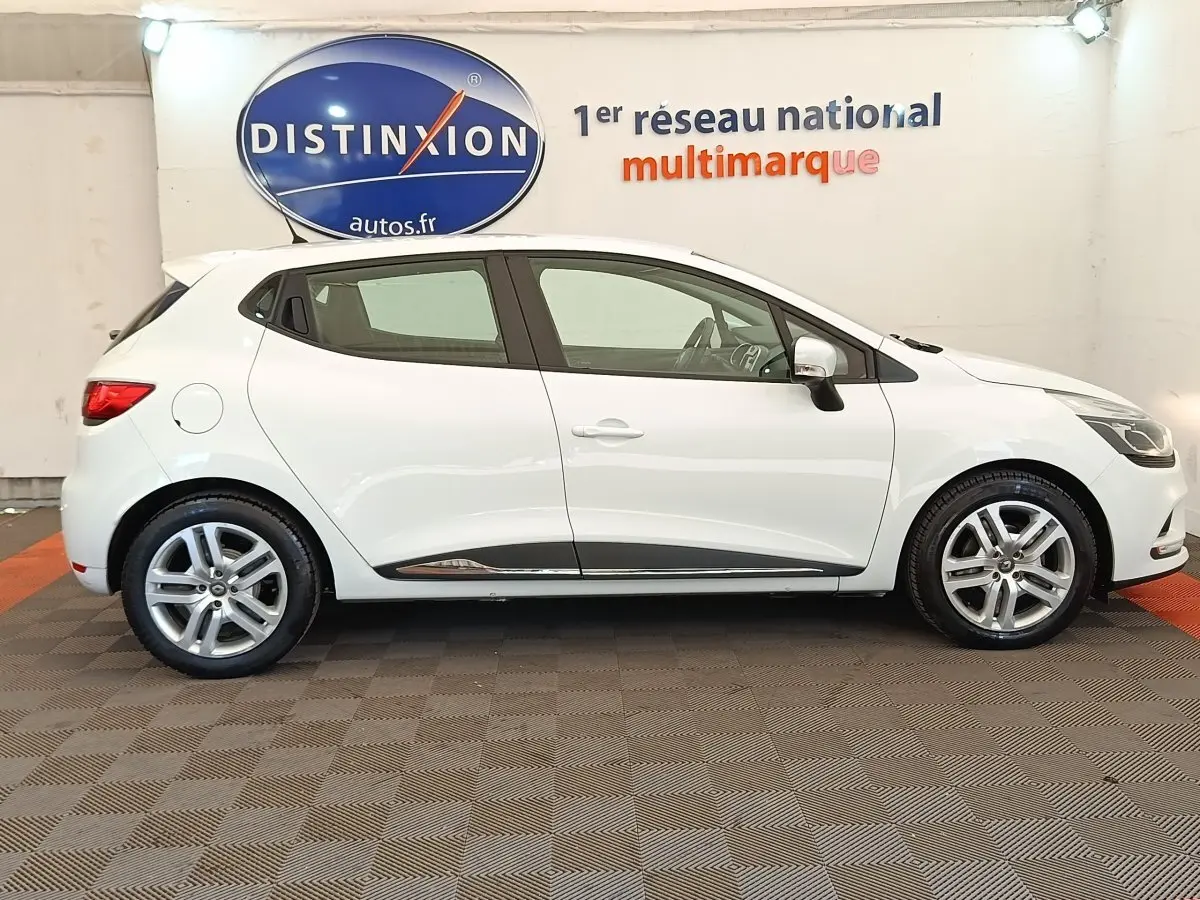 Profil droit d'une Renault Clio Business dCi 75 blanche, avec jantes alliage et rétroviseurs électriques dans un showroom.