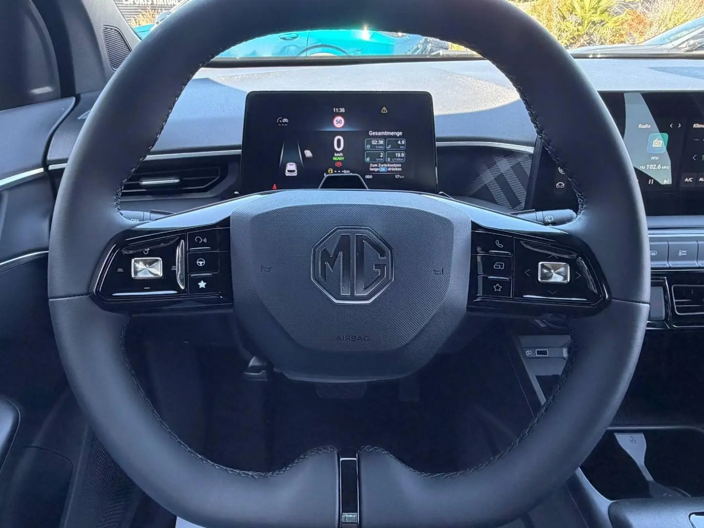 Vue centrée sur le volant cuir multifonction avec logo MG, tableau de bord numérique et écran tactile en arrière-plan.