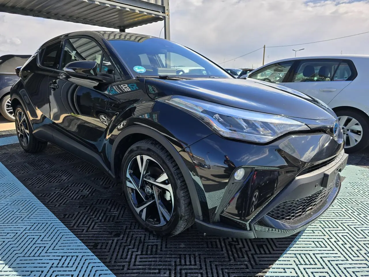 Toyota C-HR noir métal vu en 3/4 avant droit, avec jantes alliage 18 pouces et optiques LED distinctives.