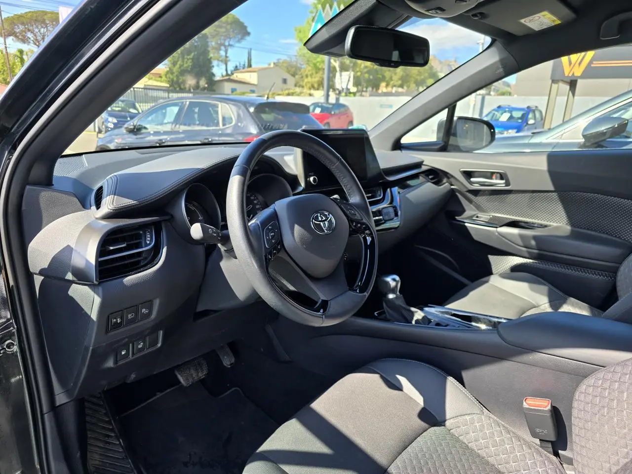 Intérieur côté conducteur du Toyota C-HR noir métal 2023, volant cuir multifonction et écran tactile central visible.
