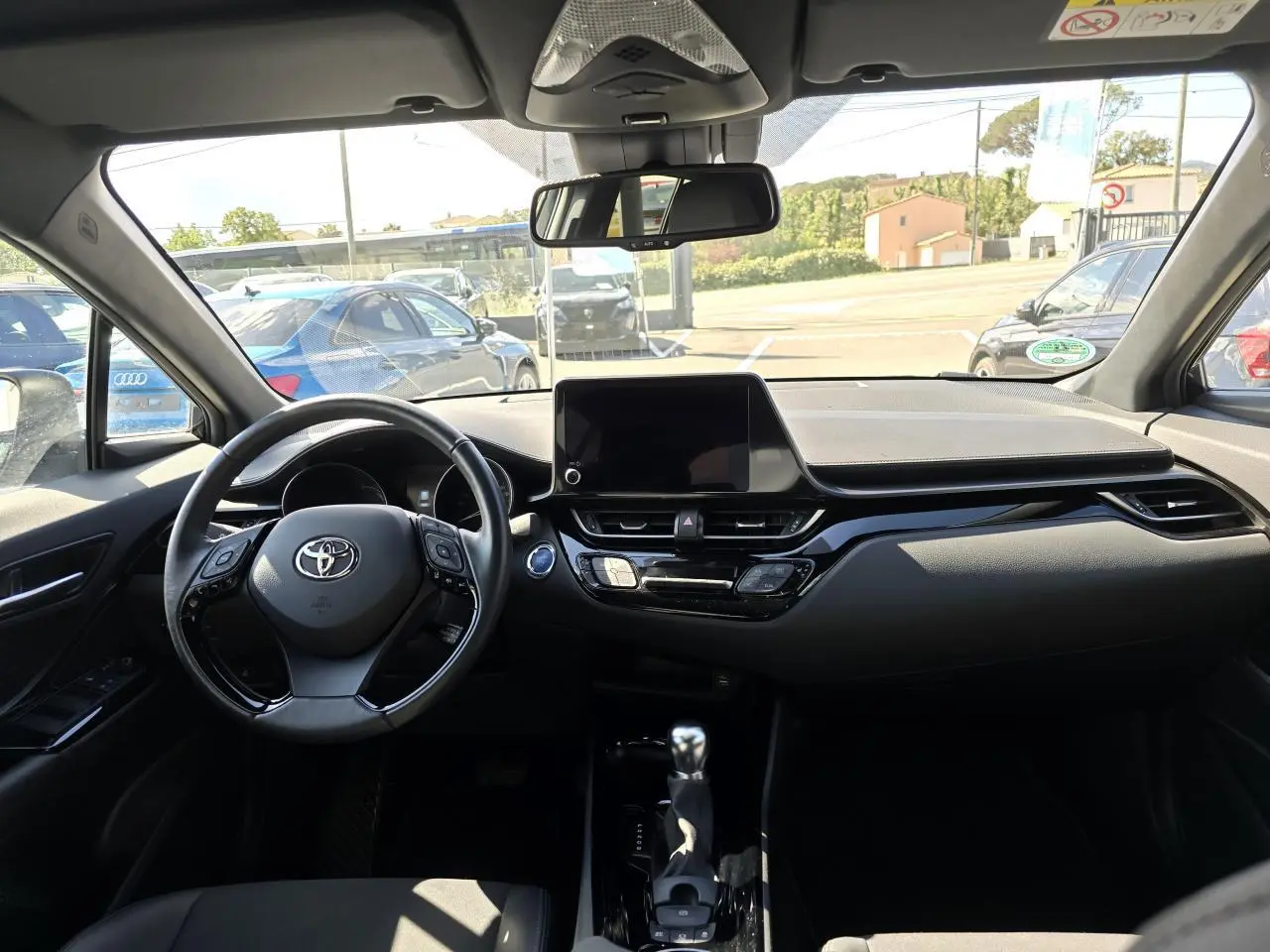 Vue intérieure avant du Toyota C-HR 1.8 Hybride 2023 avec tableau de bord noir et écran tactile central.