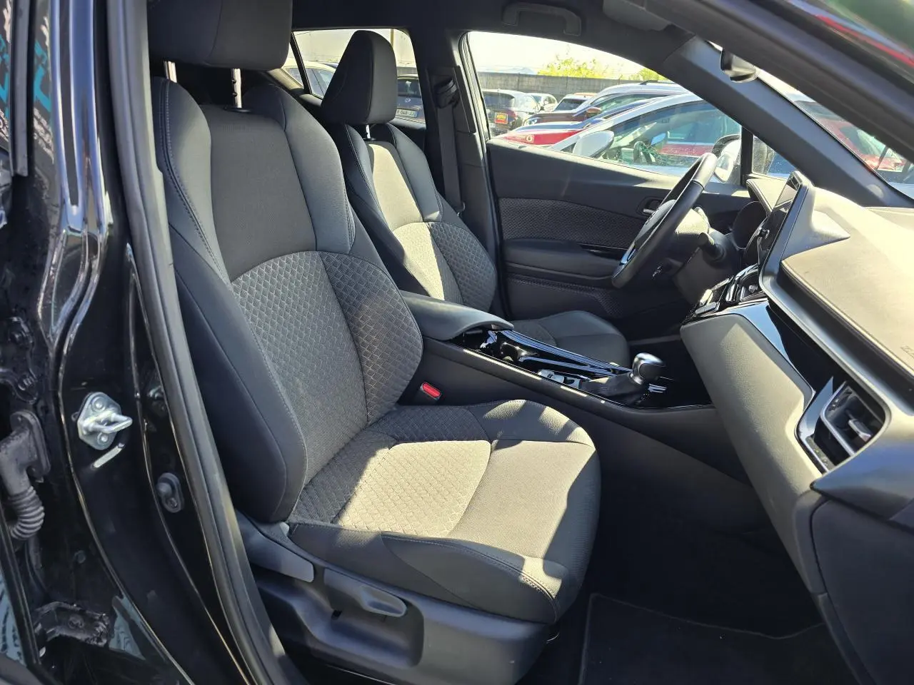 Intérieur côté conducteur du Toyota C-HR noir métal 2023, sièges tissu/cuir avec surpiqûres grises et console centrale brillante.