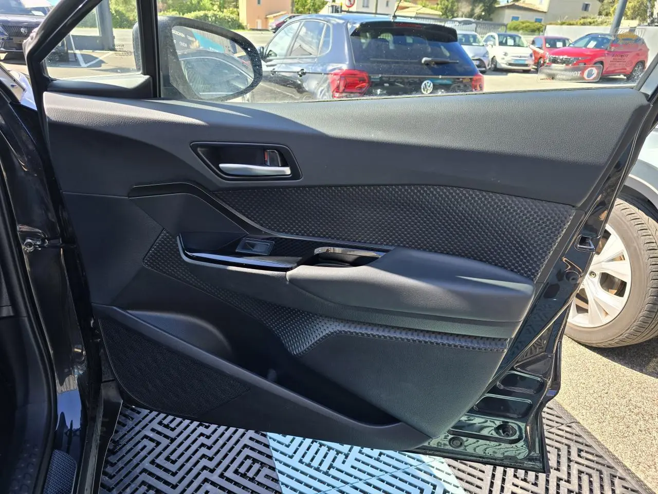 Porte avant gauche ouverte d'un Toyota C-HR noir métal, montrant le panneau intérieur avec poignée et commande de vitre.