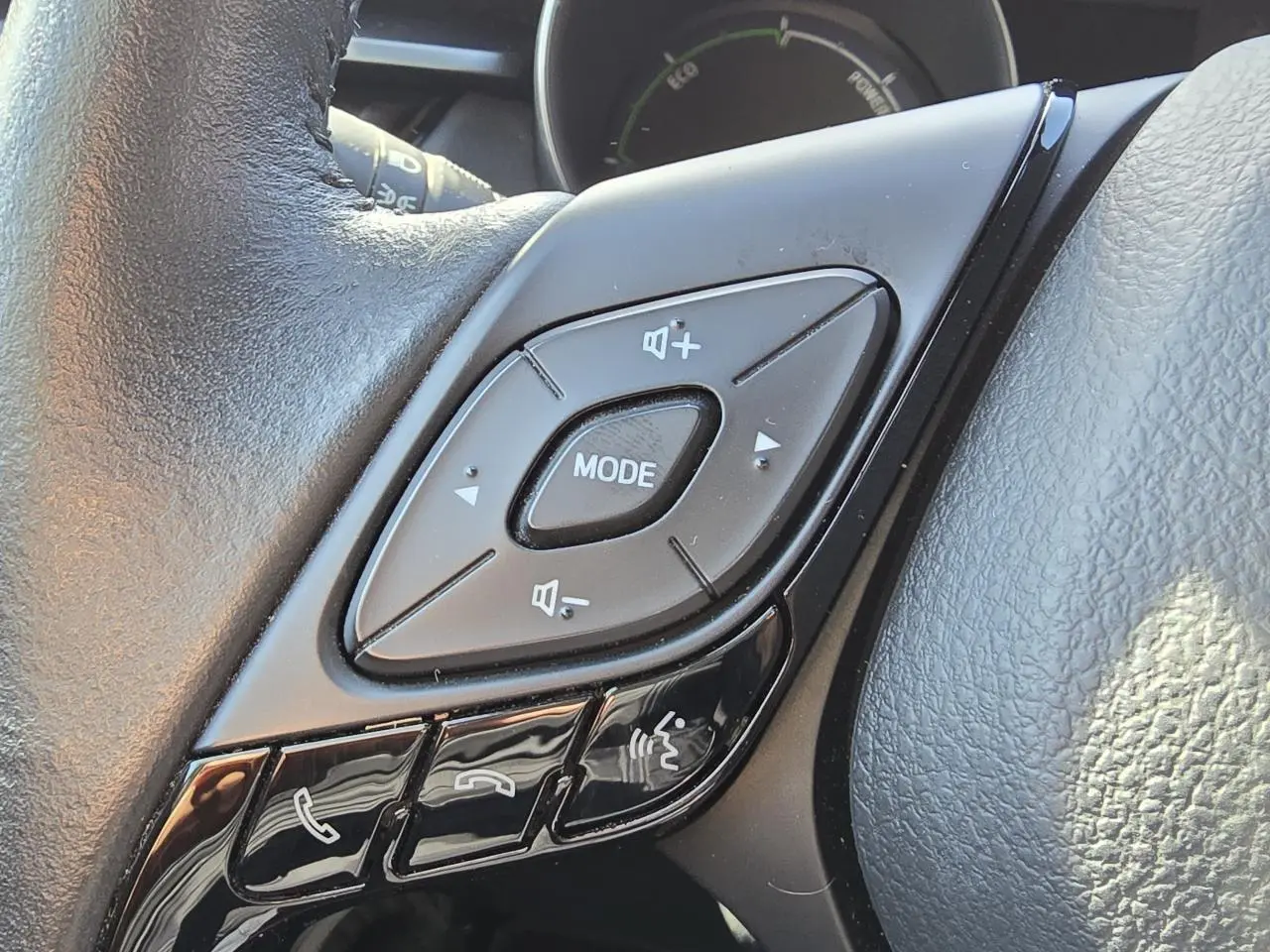 Gros plan sur les commandes multifonctions du volant cuir noir du Toyota C-HR 1.8 Hybride 2023.