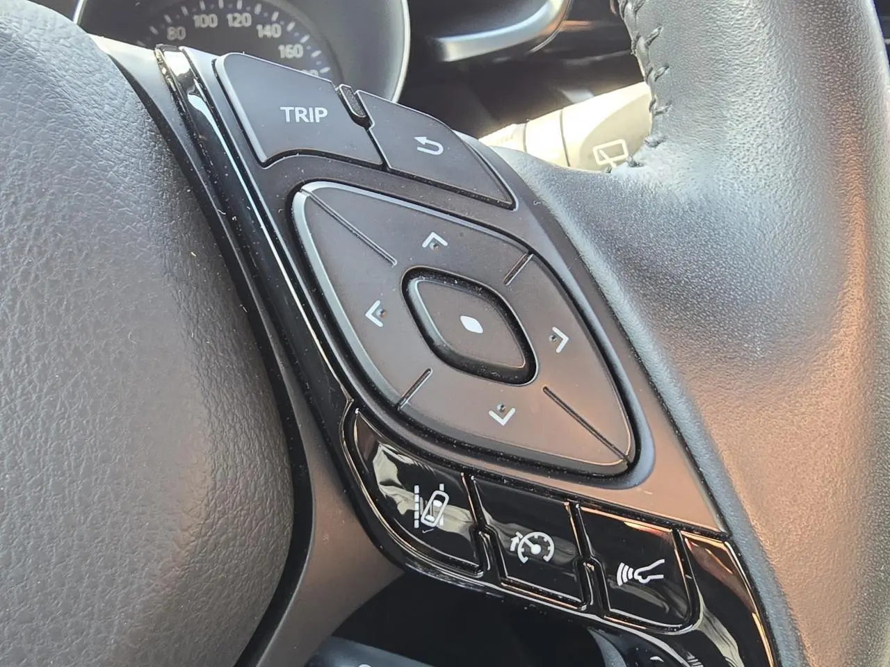 Gros plan sur les commandes multifonctions noires du volant cuir du Toyota C-HR 1.8 Hybride noir métal 2023.