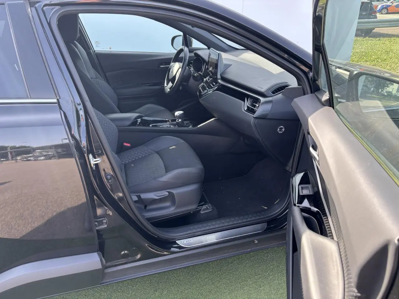 Intérieur côté gauche d'une Toyota C-HR noir métal 2023, sièges tissu/cuir noir avec surpiqûres grises et tableau de bord moderne.