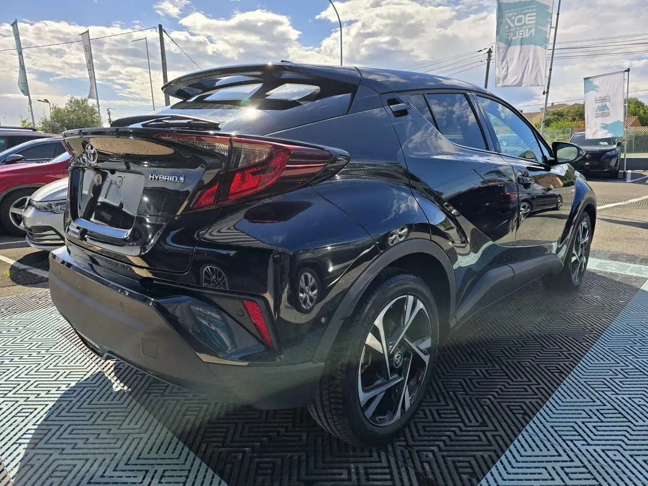 Toyota C-HR noir métal vu en 3/4 arrière droit, avec jantes alliage 18 pouces et becquet avant couleur carrosserie.