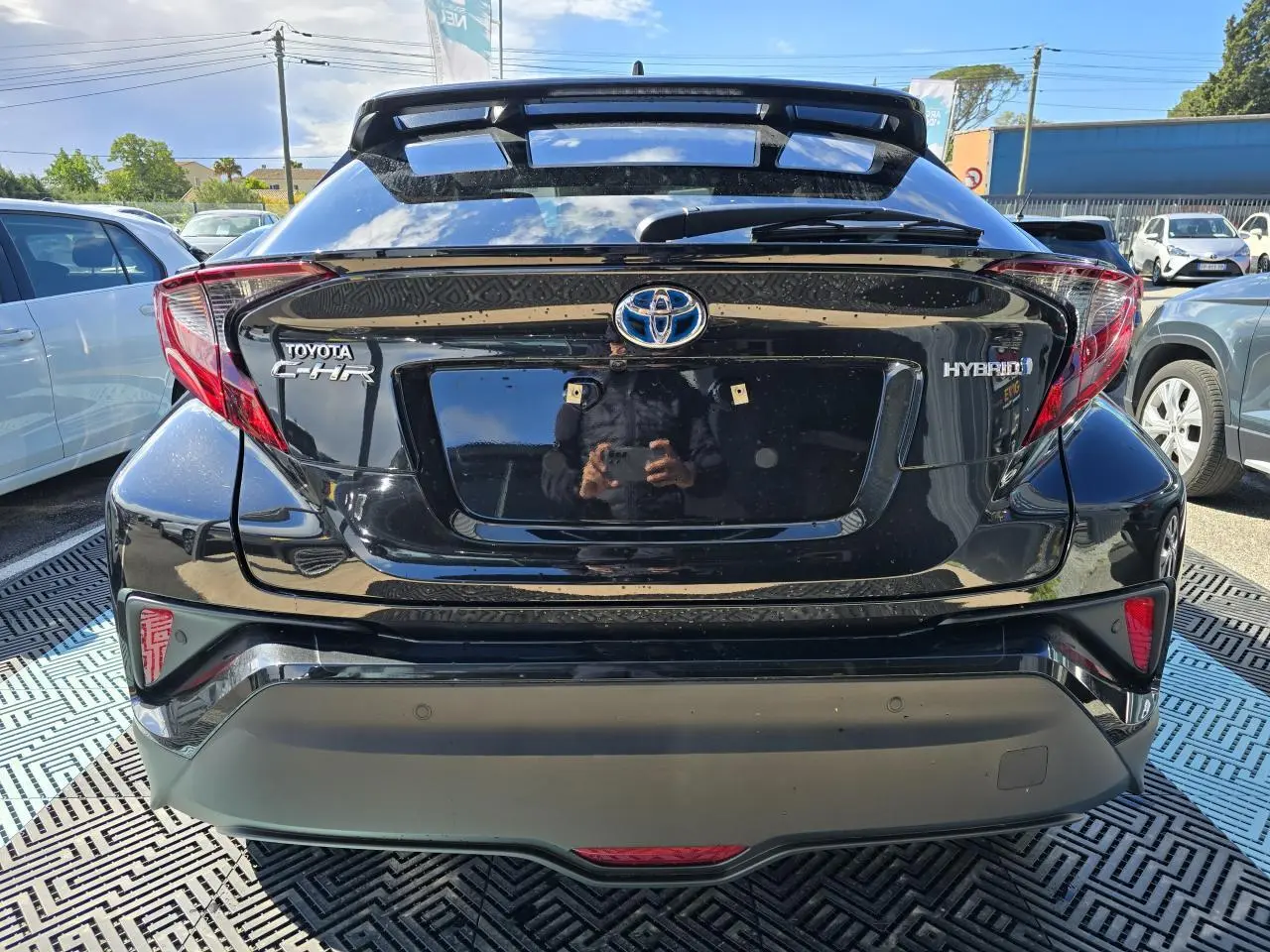 Vue arrière d'un Toyota C-HR noir métal hybride 2023 avec becquet et feux arrière distinctifs en forme angulaire.