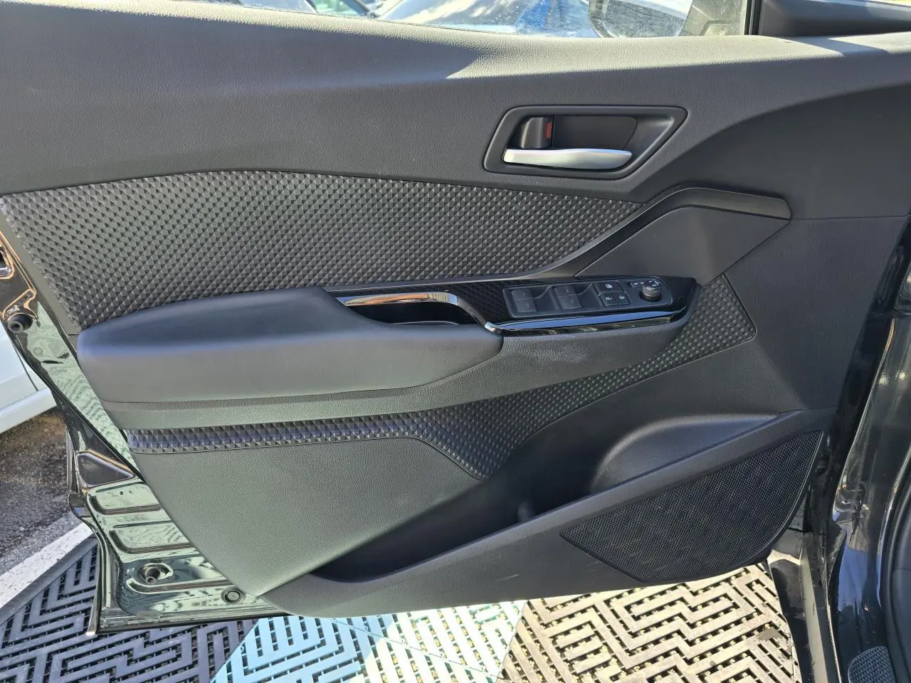 Porte avant gauche ouverte du Toyota C-HR noir métal 2023, avec commandes électriques et garniture texturée.