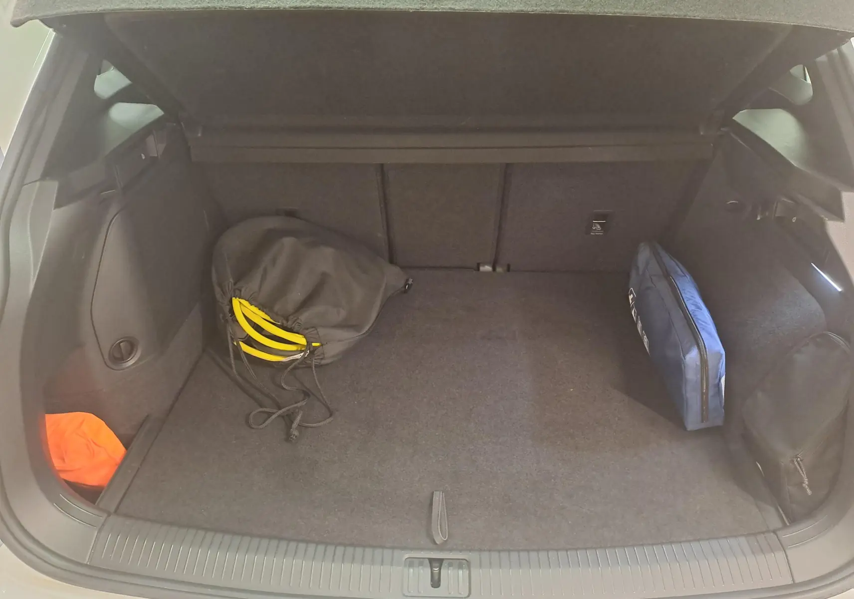 Coffre ouvert du Volkswagen Tiguan 1.4 eHybrid blanc pur 2023, montrant un sac noir et une trousse bleue à l'intérieur.