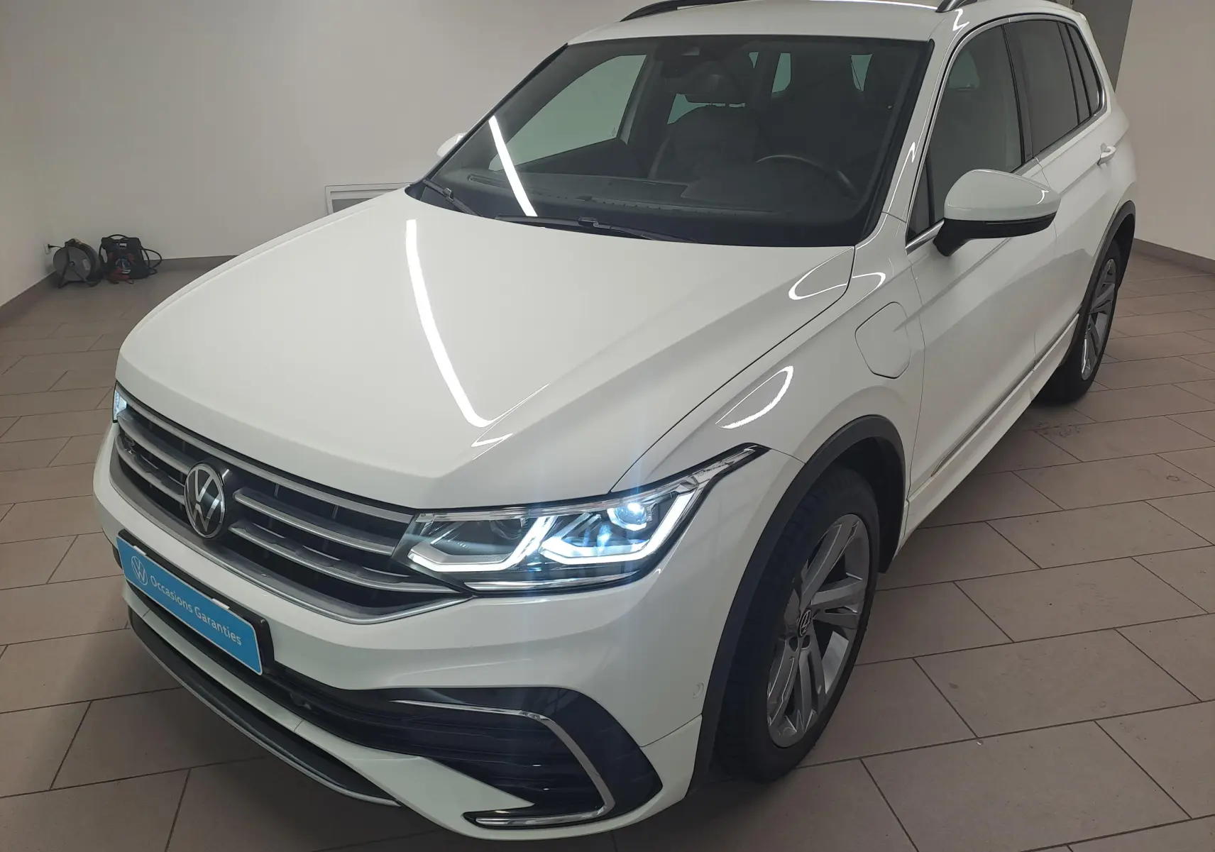 Volkswagen Tiguan 1.4 eHybrid R-Line blanc pur vu en 3/4 avant droit avec phares LED allumés dans un intérieur neutre.