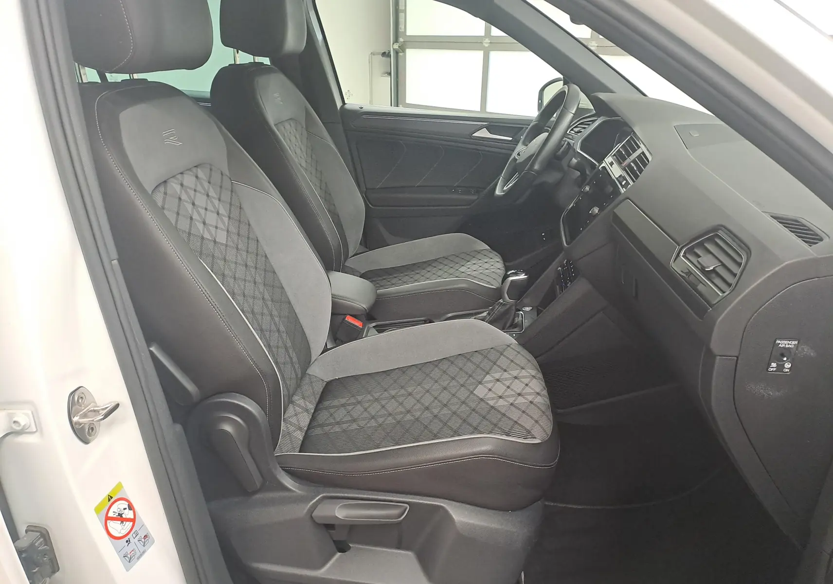 Vue intérieure côté conducteur du Volkswagen Tiguan 1.4 eHybrid 2023 blanc pur, sièges R-Line en tissu noir et gris à motifs.