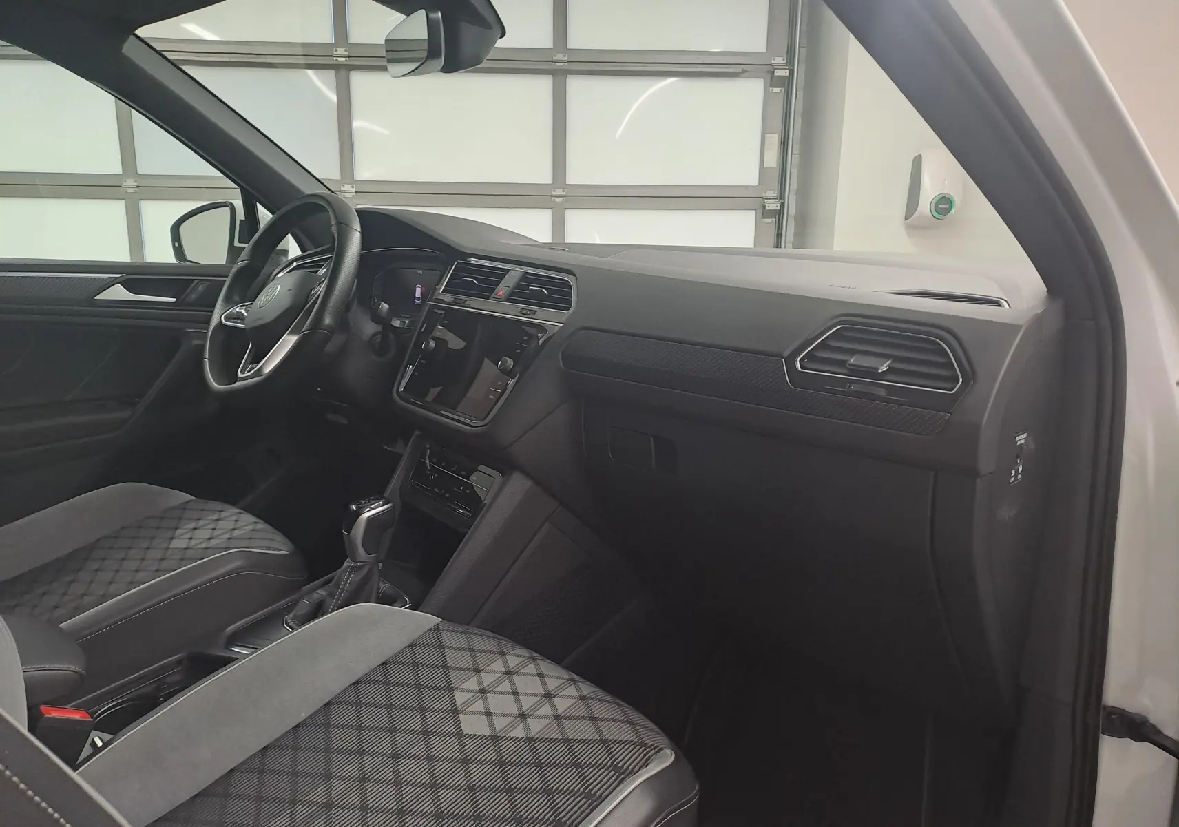 Intérieur côté conducteur du Volkswagen Tiguan 1.4 eHybrid blanc, avec tableau de bord moderne et sièges tissu à motif géométrique.