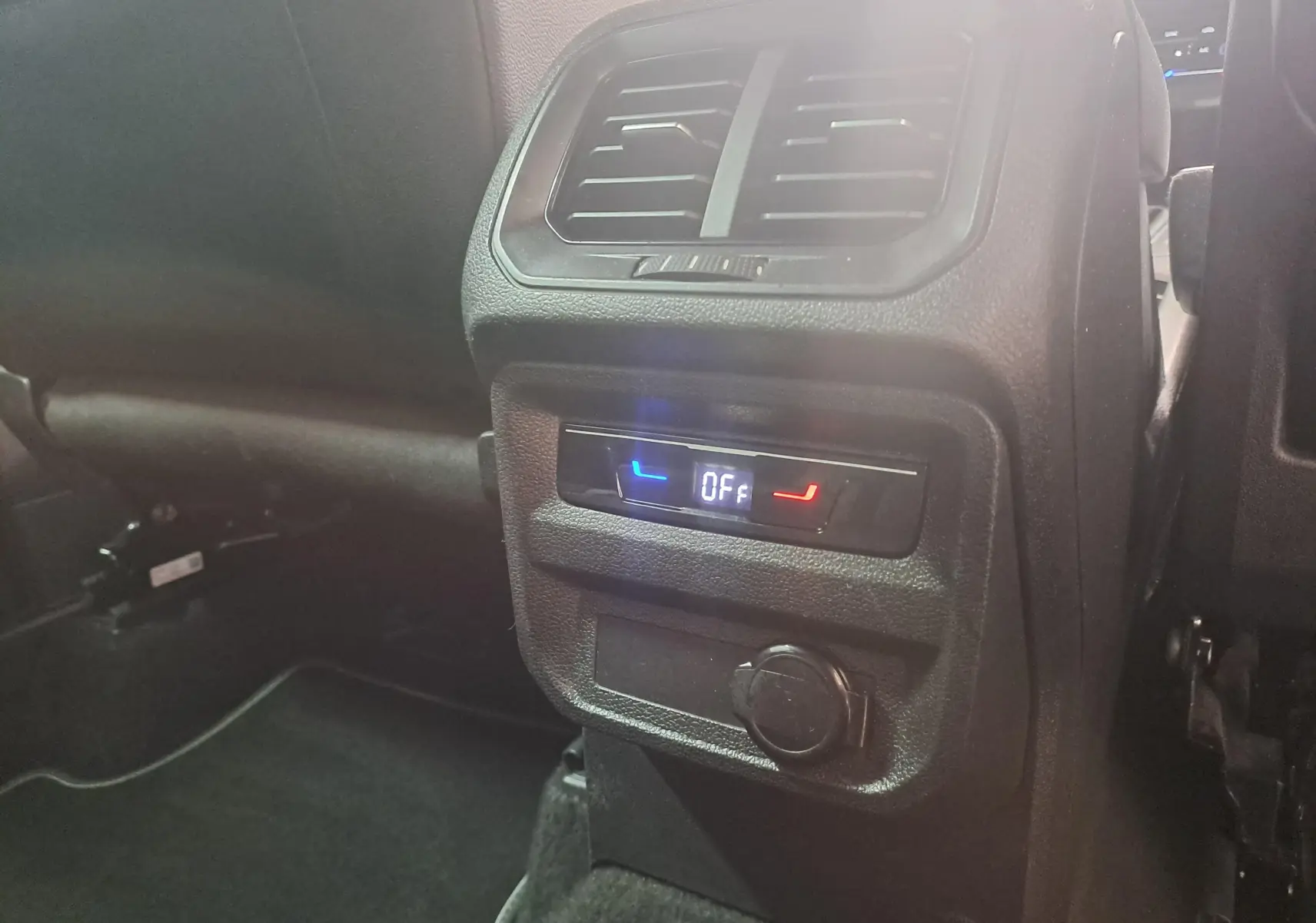Détail de la console arrière noire du Volkswagen Tiguan 1.4 eHybrid 2023 avec commandes climatisation et prise 12V.