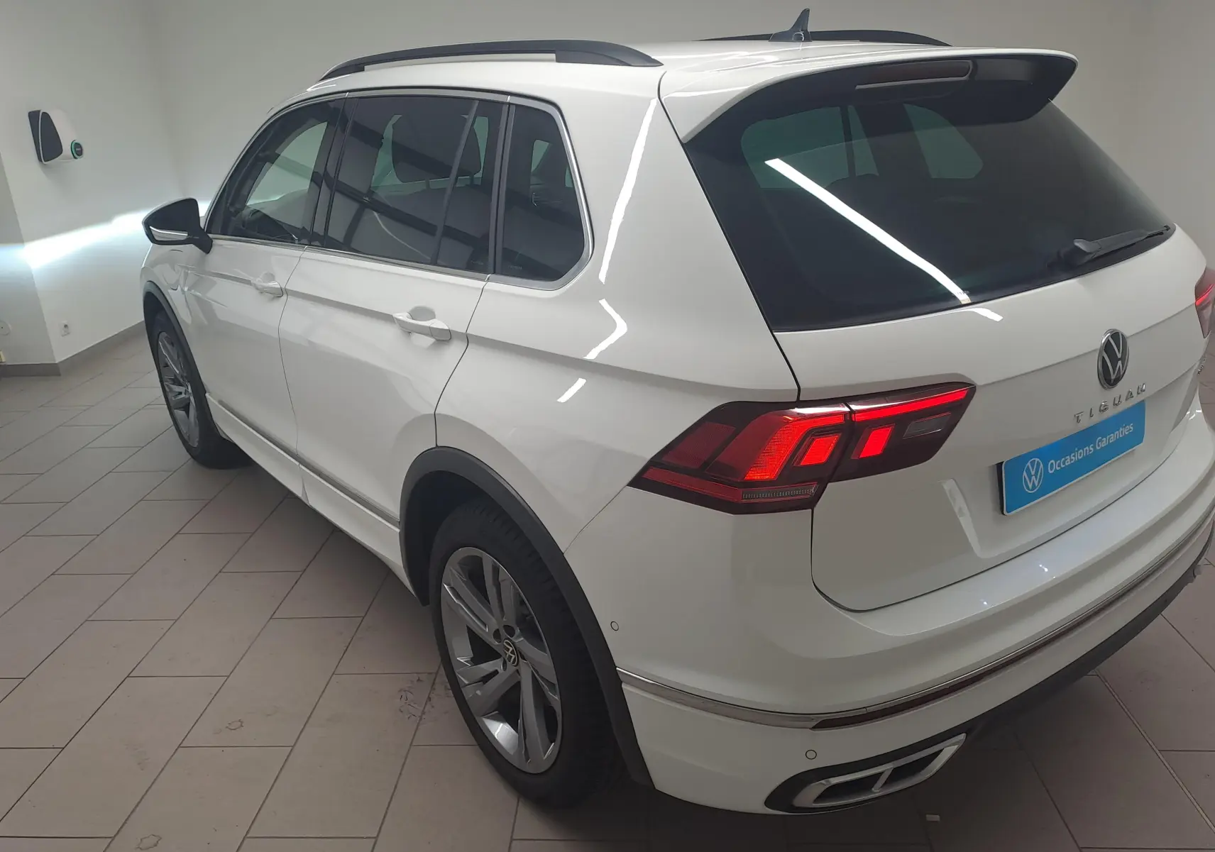 Vue 3/4 arrière droite du Volkswagen Tiguan blanc pur 2023 R-Line avec feux arrière allumés en intérieur showroom.