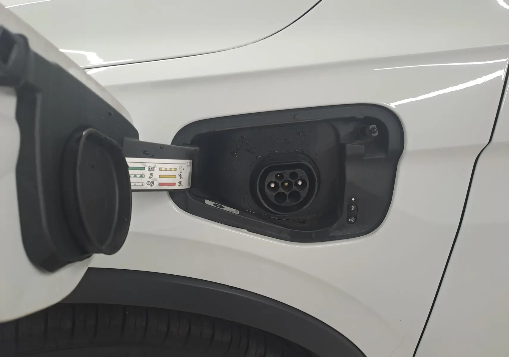 Prise de recharge ouverte côté avant gauche du Volkswagen Tiguan blanc pur 2023 hybride rechargeable R-Line.