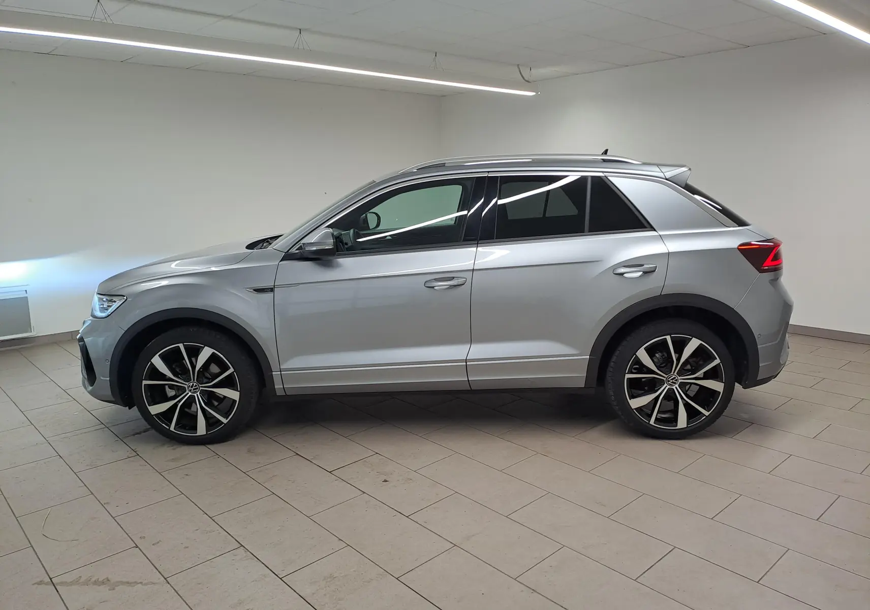 Vue de profil côté gauche d'un Volkswagen T-Roc 2025 gris pyrite avec jantes alliage 19'' noires et feux arrière LED.