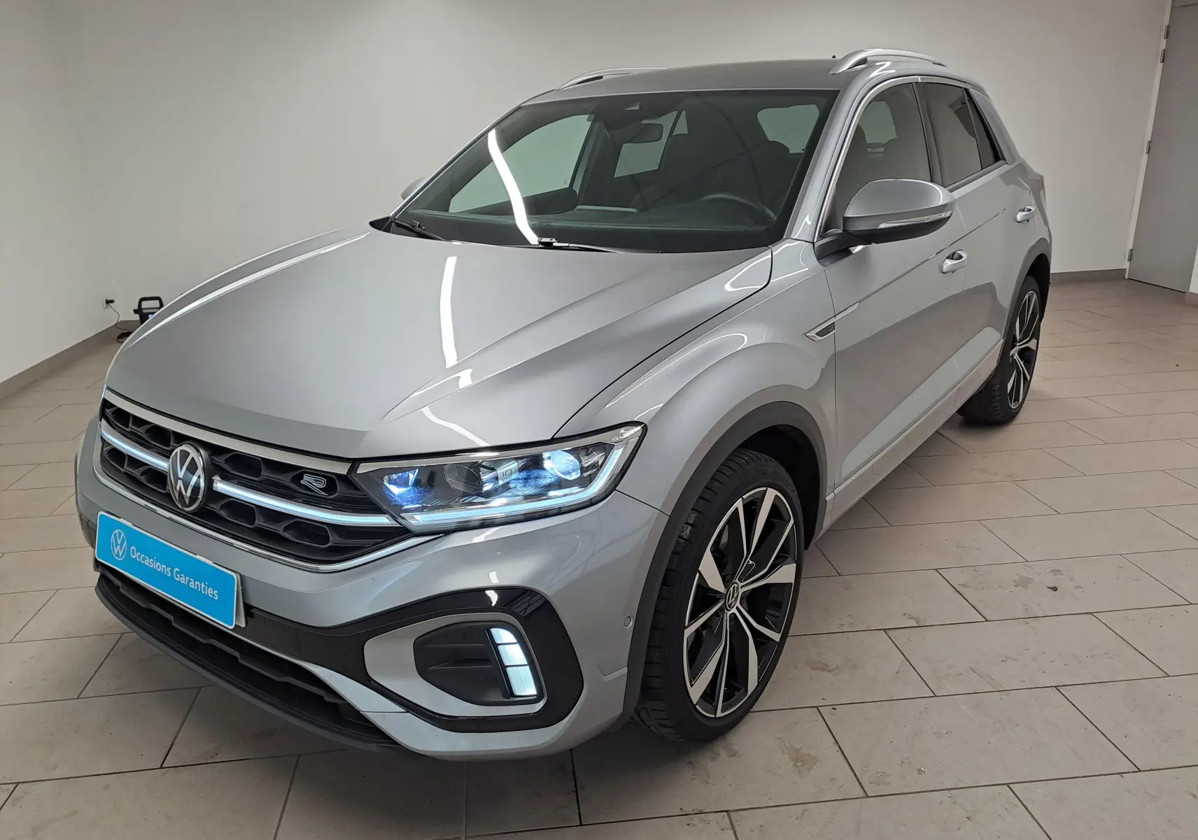 Volkswagen T-Roc 1.5 TSI R-Line gris pyrite en 3/4 avant droit avec phares Matrix LED allumés et jantes 19'' noires.