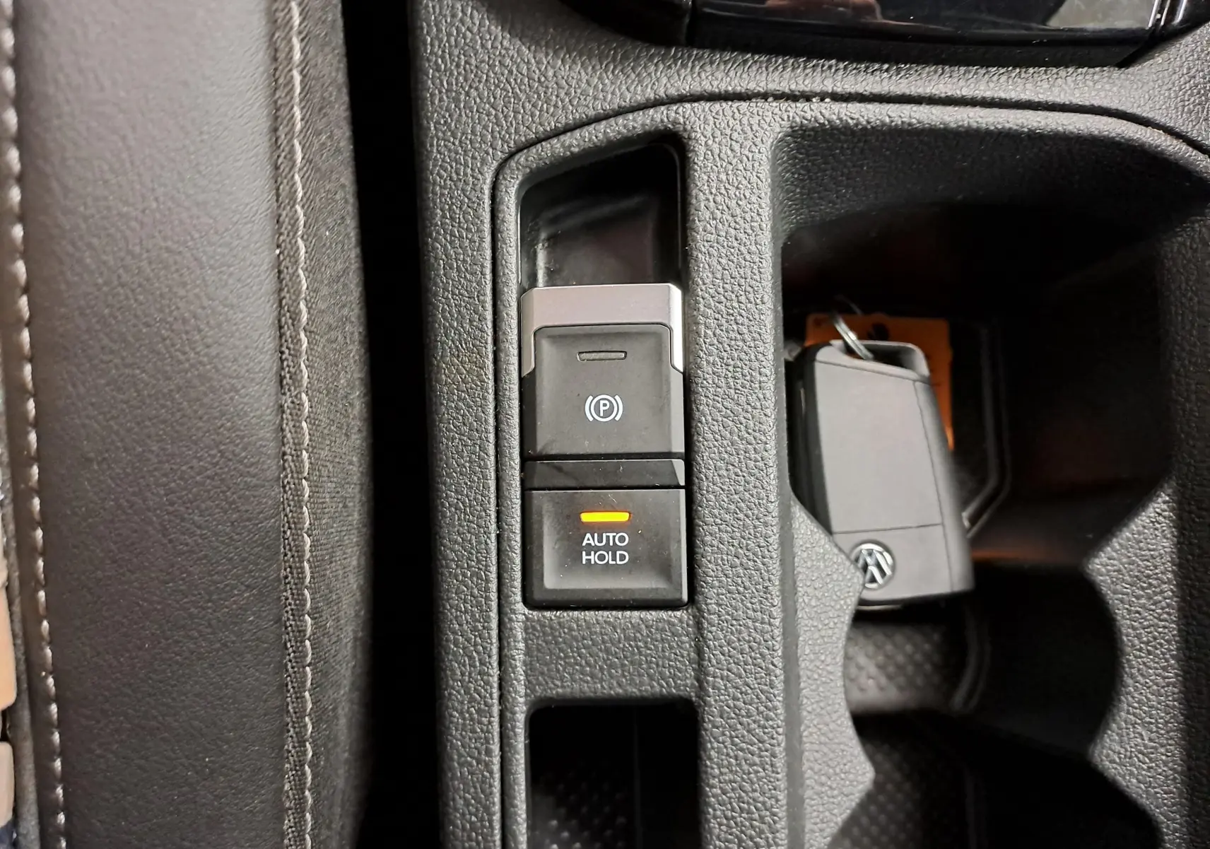 Gros plan sur la console centrale du Volkswagen T-Roc 2025, montrant les boutons frein à main électrique et Auto Hold avec clé VW.