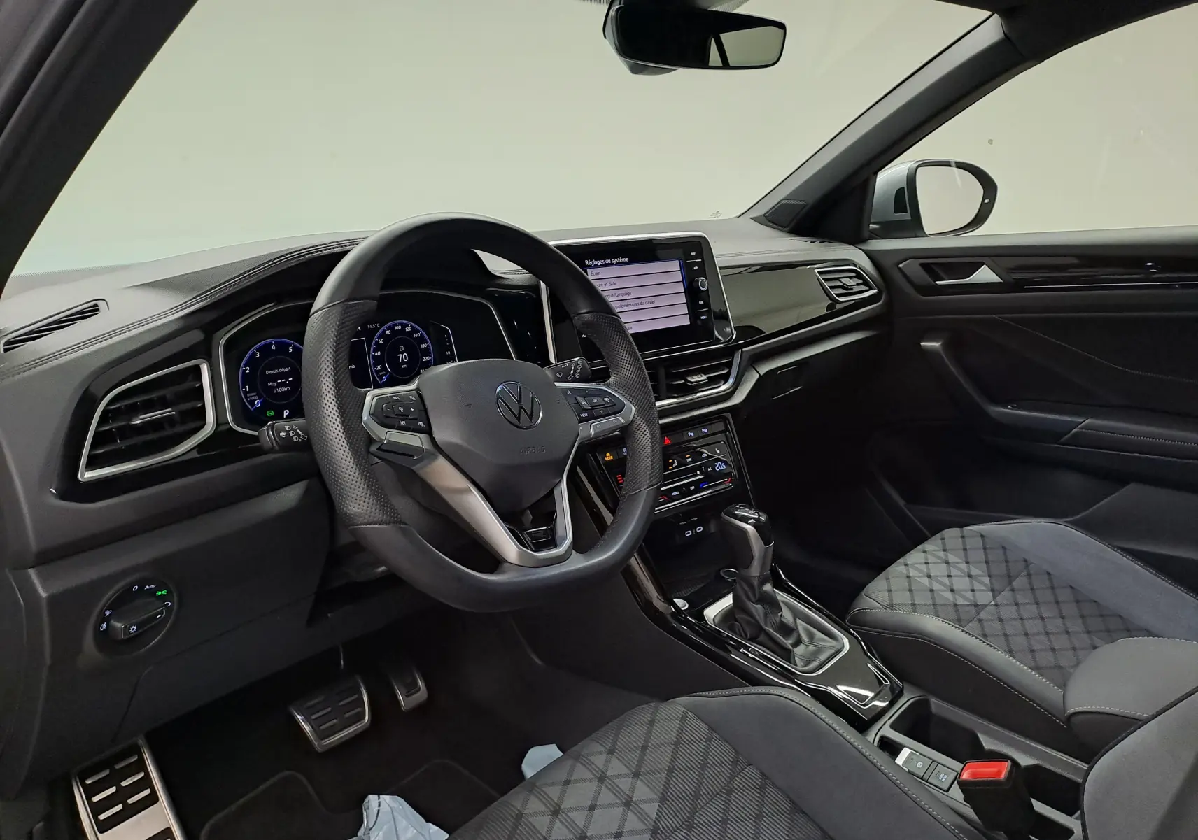 Vue intérieure côté conducteur du Volkswagen T-Roc 1.5 TSI 150 DSG7 R-Line Edition avec volant multifonction et sellerie tissu noire.