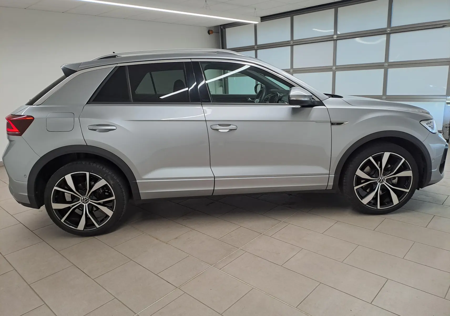 Vue de profil côté gauche d'un Volkswagen T-Roc 2025 gris pyrite avec jantes alliage 19'' noires et vitres teintées.