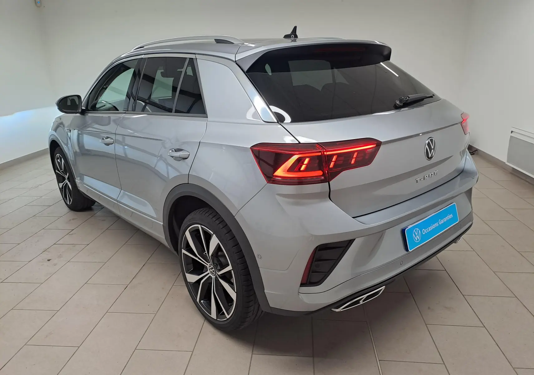 Volkswagen T-Roc gris pyrite en 3/4 arrière droit, avec feux LED allumés et jantes alliage noires 19 pouces.