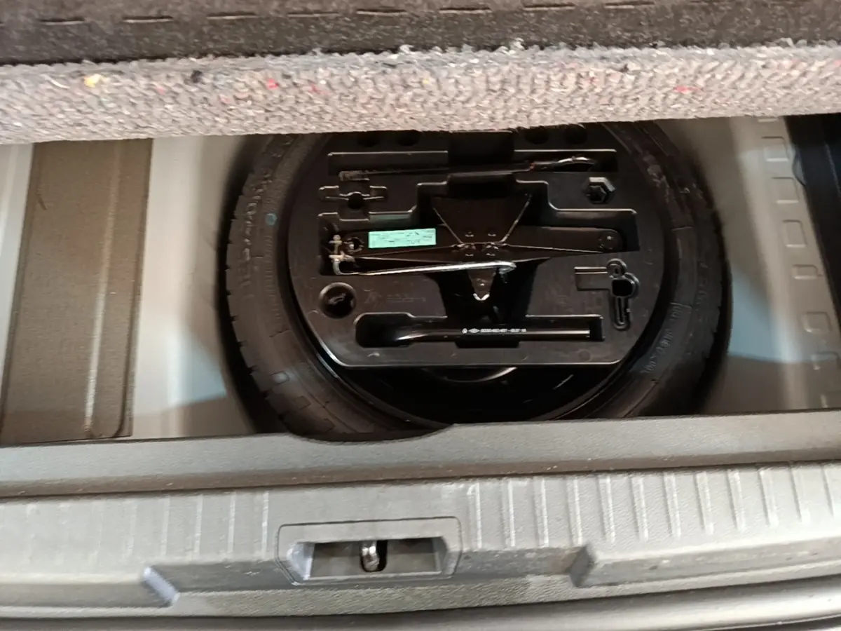 Vue rapprochée du coffre ouvert du Renault Captur gris clair 2018, montrant la roue de secours et son outillage.
