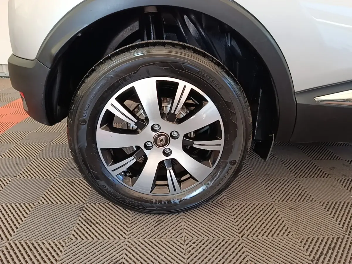 Gros plan sur la roue avant gauche d’un Renault Captur gris clair, avec jante alliage à cinq branches doubles.