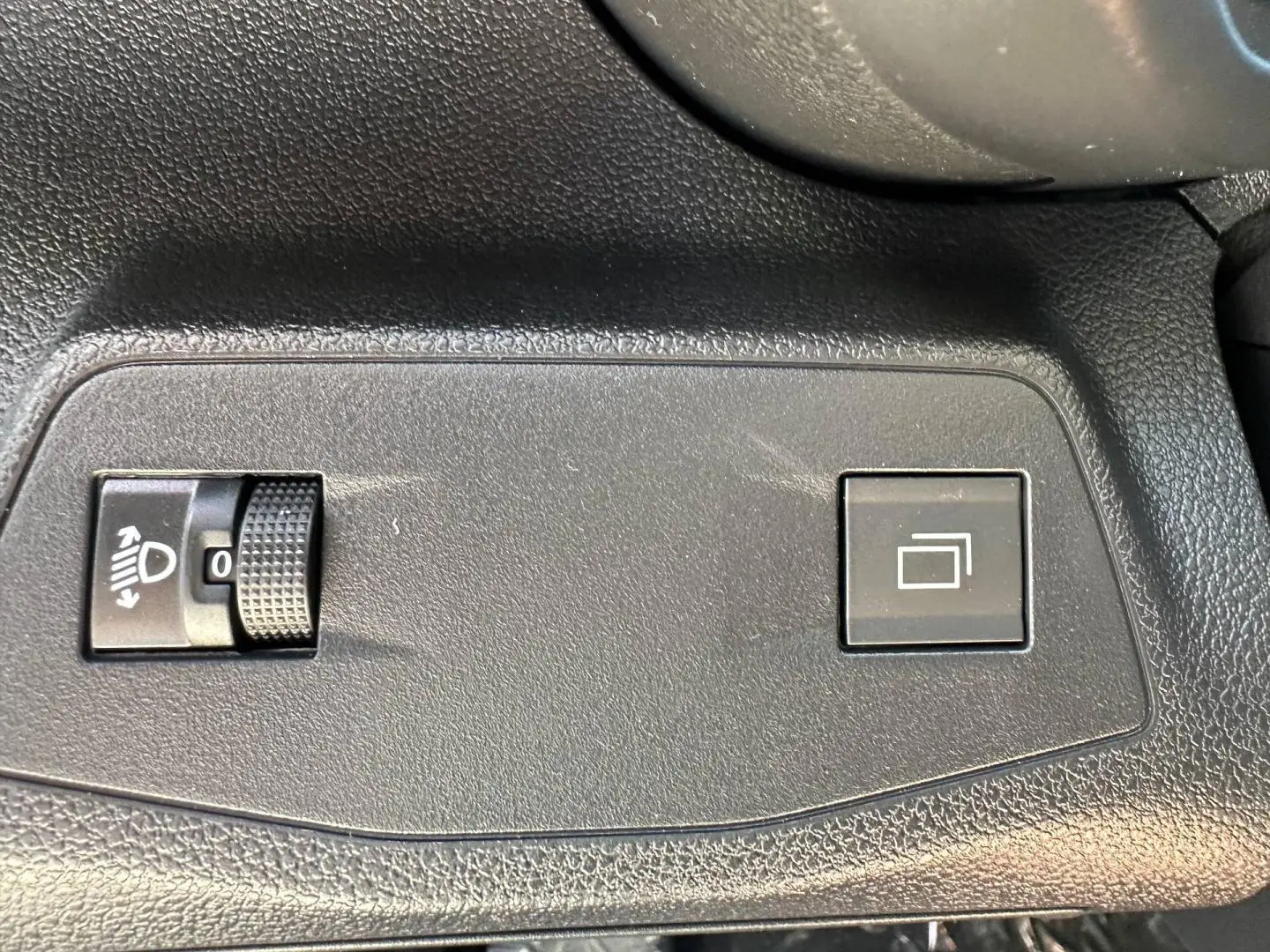 Détail intérieur montrant les commandes de réglage des phares et de l'affichage sur plastique noir texturé du Citroën Berlingo Kiama Blue.