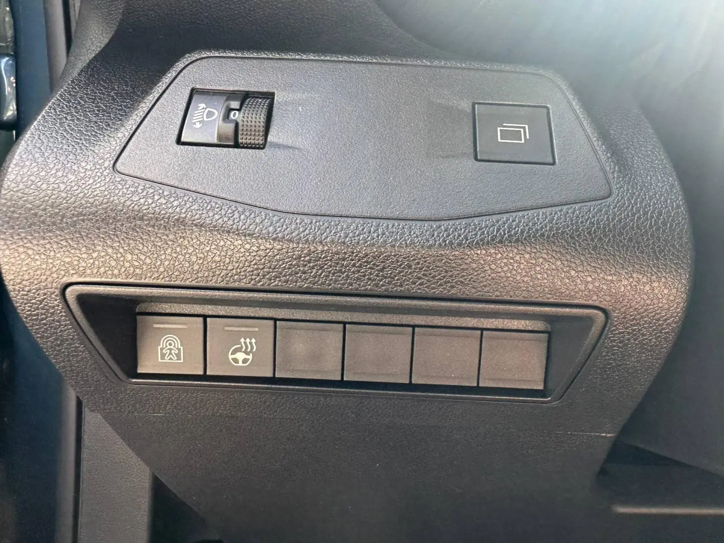 Gros plan sur les commandes de réglage des phares et du volant chauffant à gauche du tableau de bord du Citroën Berlingo bleu.