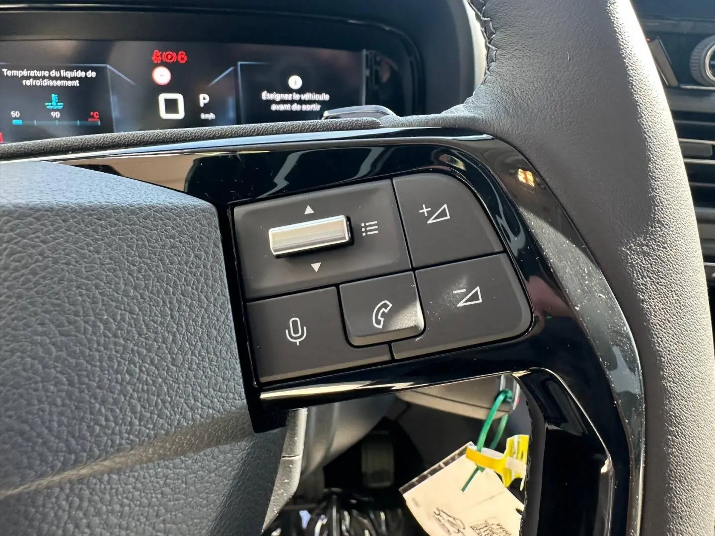 Gros plan sur les commandes multifonctions noires du volant cuir du Citroën Berlingo 2026, avec affichage digital en arrière-plan.