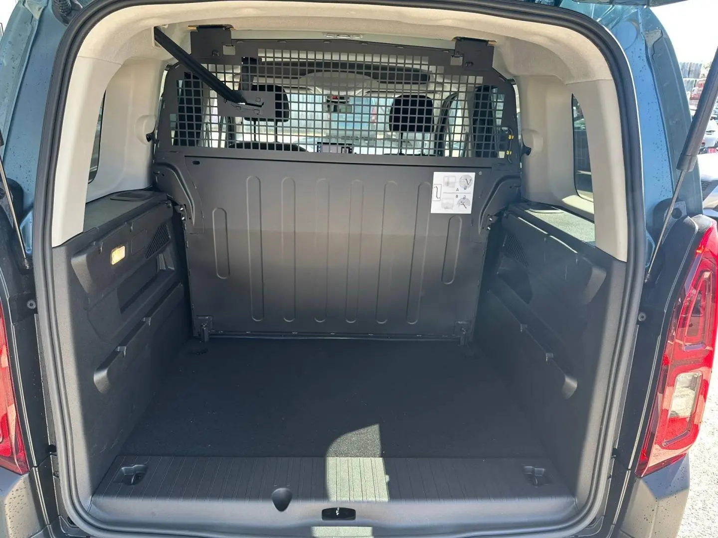 Coffre ouvert vu de l'arrière d'un Citroën Berlingo Kiama Blue avec séparation métallique et espace de chargement vide.