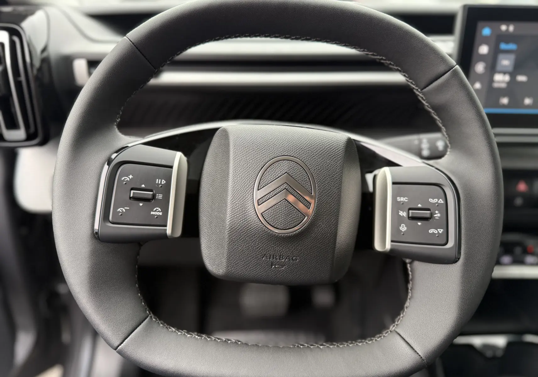 Gros plan sur le volant cuir noir du Citroën C3 hybride 2026, avec commandes intégrées et logo central chromé.