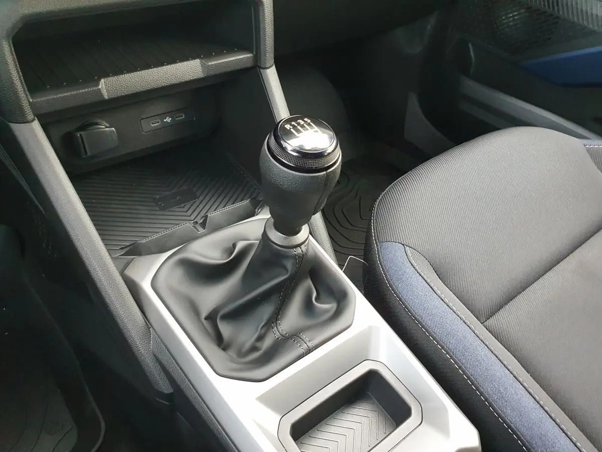 Gros plan intérieur sur le levier de vitesses manuel et la console centrale du Dacia Duster 2025, sièges tissu noir et bleu.