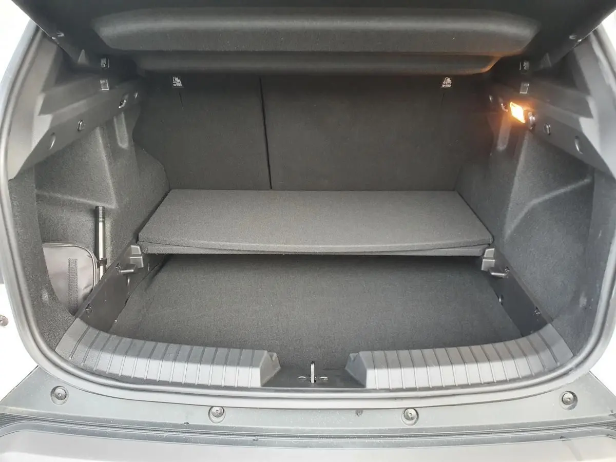 Vue intérieure du coffre du Dacia Duster blanc glacier 2025, avec tablette de rangement et éclairage latéral allumé.