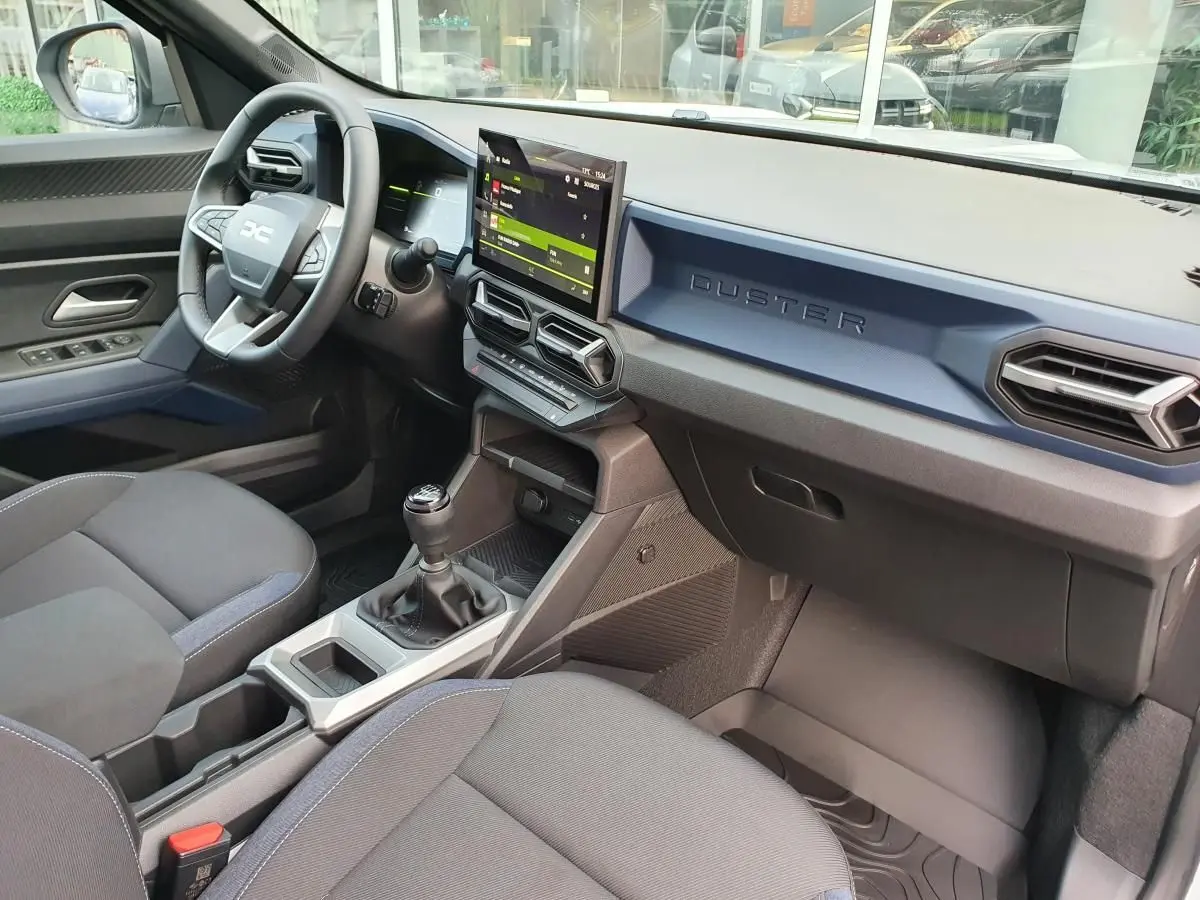 Vue intérieure côté conducteur du Dacia Duster 2025, tableau de bord bleu, écran tactile et levier de vitesses manuel visible.