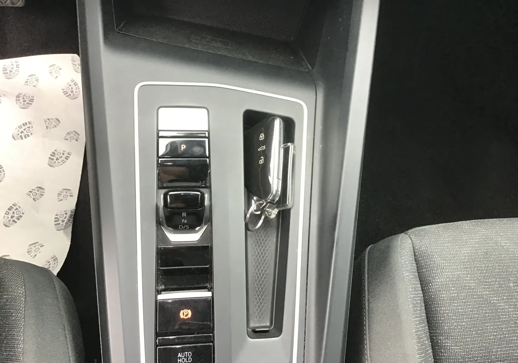 Vue plongeante sur la console centrale grise de la Volkswagen Golf VIII avec levier de vitesses DSG7 et clé mains libres posée.
