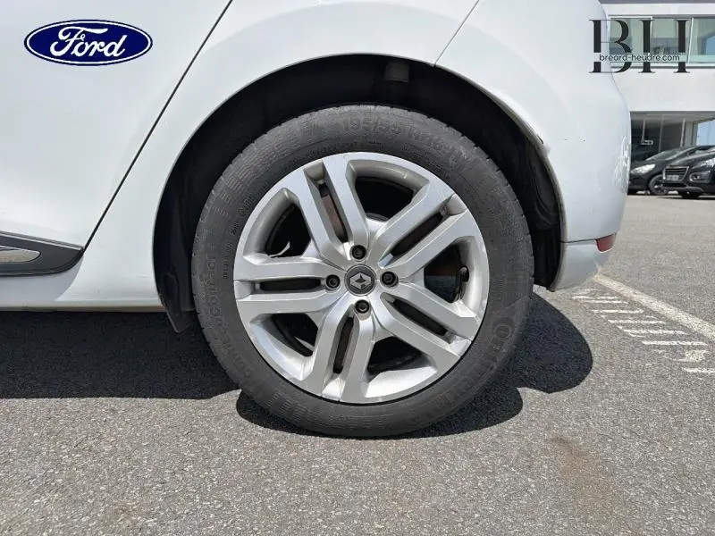 Gros plan sur la roue avant droite d'une Renault Clio blanche, avec jante en alliage et logo Renault au centre.