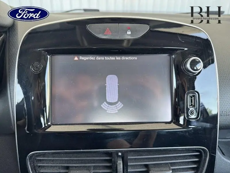 Écran tactile central noir montrant l'alerte radar de recul dans l'habitacle d'une Renault Clio blanche.
