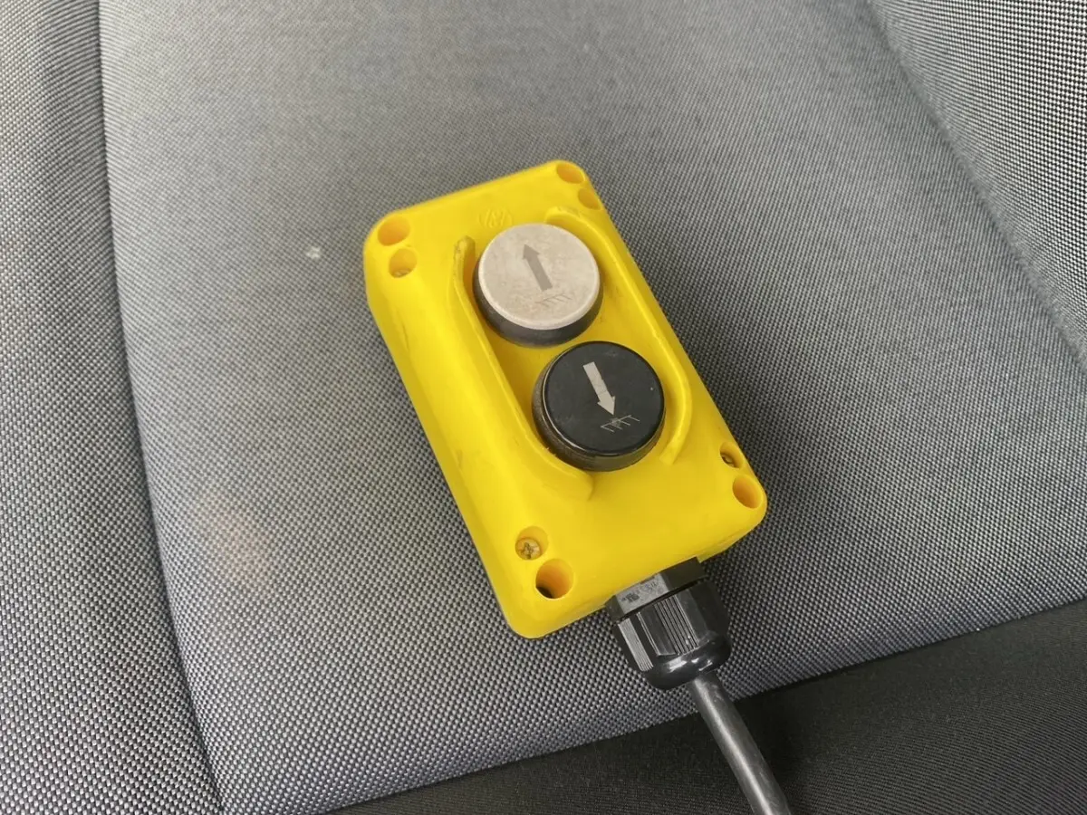 Gros plan sur la télécommande jaune avec deux boutons fléchés, posée sur un siège gris du Renault Master blanc.