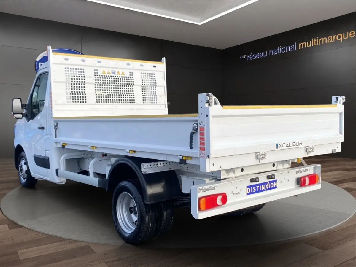 Vue 3/4 arrière droite du Renault Master blanc version benne avec ridelles et hayon, sur fond intérieur showroom.