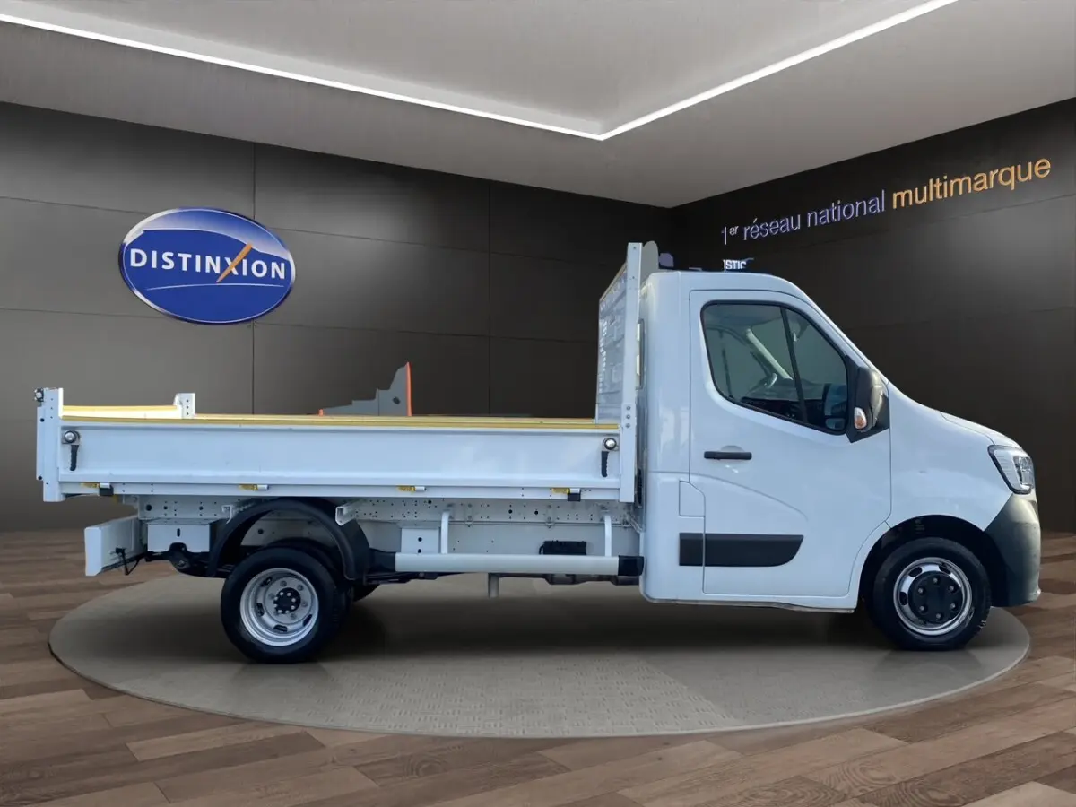 Renault Master benne blanc vu de profil côté droit dans un showroom avec sol en bois et mur noir.