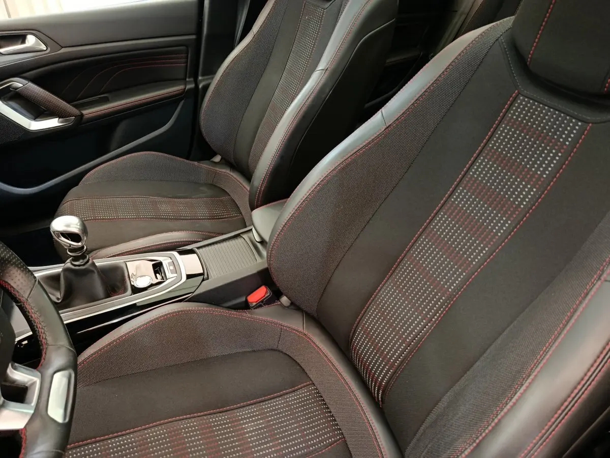 Vue intérieure rapprochée des sièges avant et levier de vitesses manuel de la Peugeot 308 GT Line avec surpiqûres rouges.