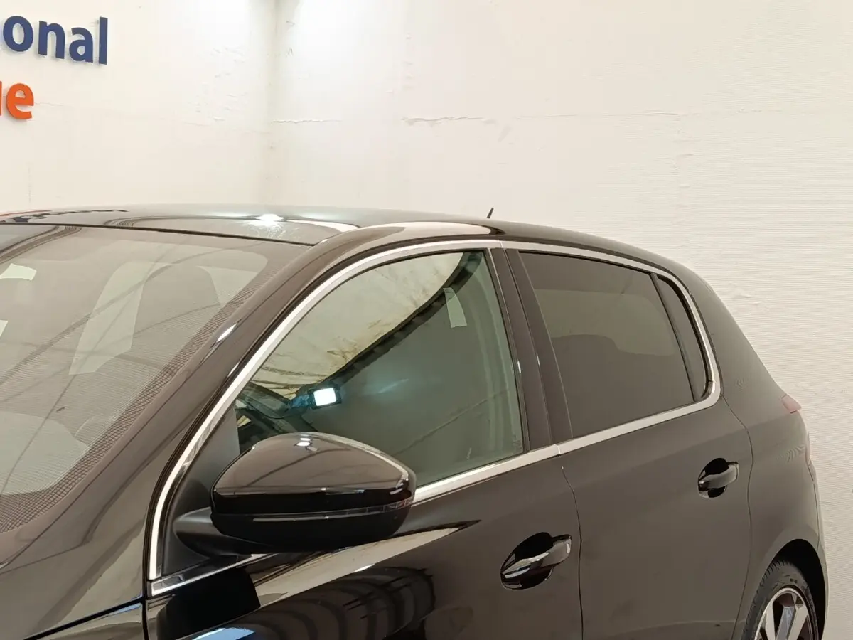 Vue côté gauche avant d'une Peugeot 308 noire 2016 avec rétroviseur ton caisse et vitres teintées.