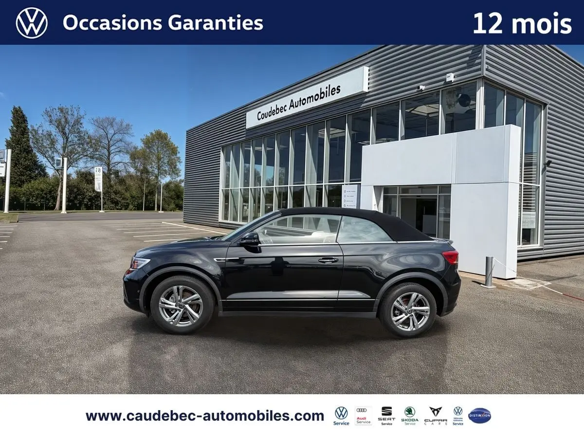 Profil droit du Volkswagen T-Roc Cabriolet noir avec capote fermée, jantes alliage et arrière du bâtiment en arrière-plan.